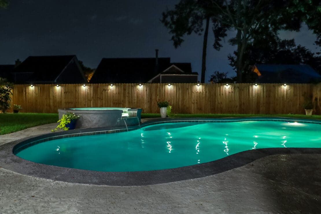 Backyard swimming pool at night with landscape lighting